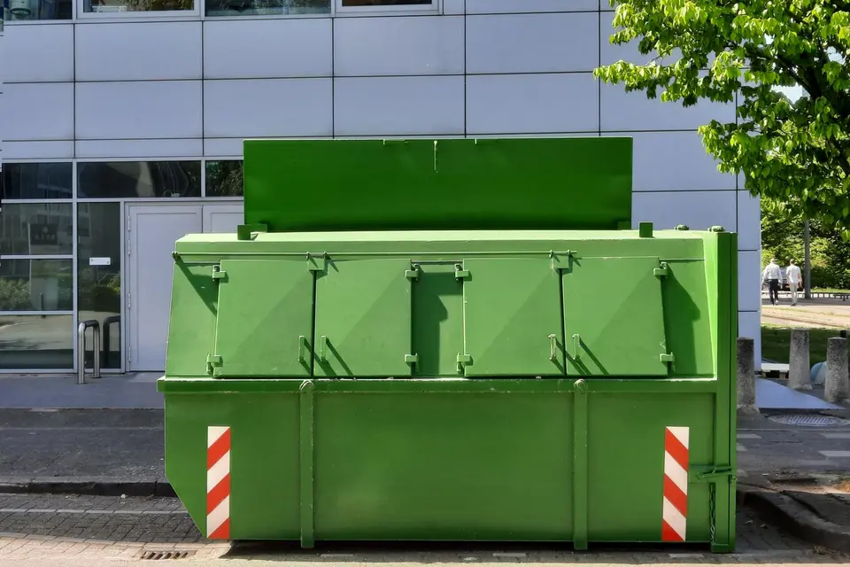 Benne verte de chantier posée sur le trottoir devant un immeuble